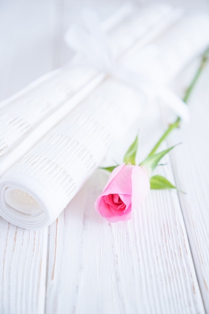 Two rolls of white fabric and pink rose on a white wooden background