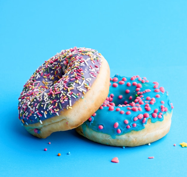 Two round baked donut with colored sugar sprinkles and with blue sugar icing