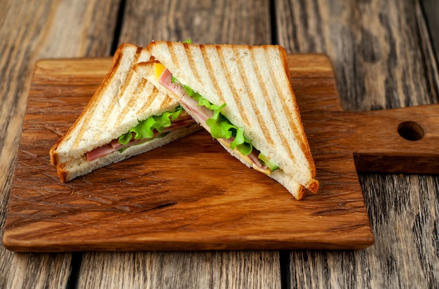 Two sandwiches on a cutting board on a wooden background in a rustic style.