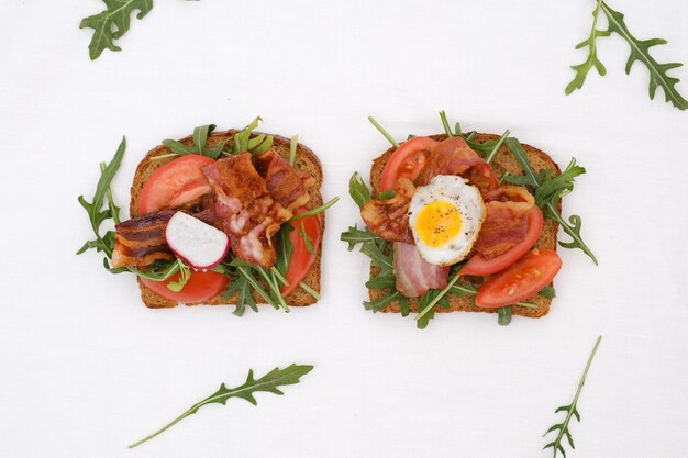 Two sandwiches with aragula fried ham tomatoes fried egg on white background top view