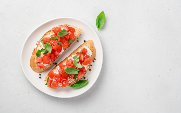 Two sandwiches with tomato, cheese, basil on a fried baguette on a gray background. Italian bruschetta. Top view.