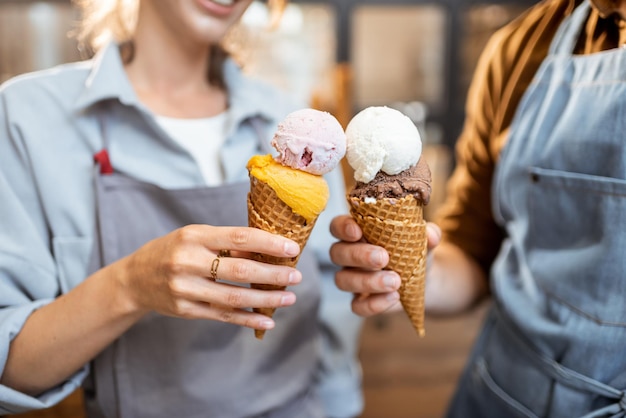 Two sellers cheering with yummy ice creams in waffle cone having fun while selling ice cream at the shop closeup