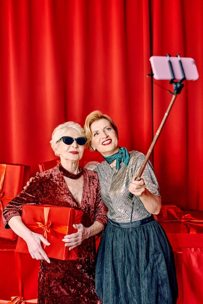 Two senior women at the party making selfie holding cellphone on selfie stick. Party, celebration,