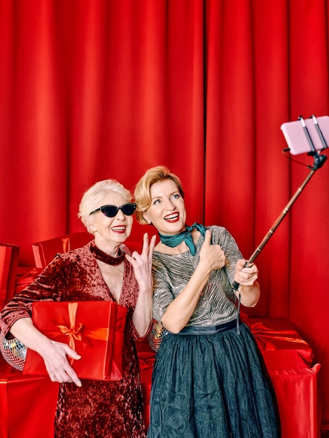 Two senior women at the party making selfie holding cellphone on selfie stick. Party, celebration,