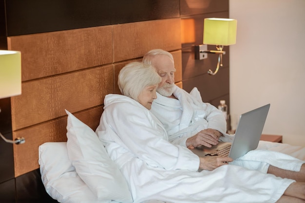 Two seniors watching something on laptop and looking interested