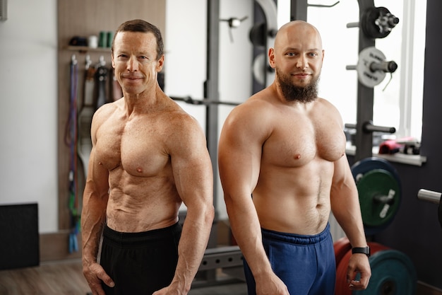 Two shirtless men standing in gym young man and his senior father exercise together in gym