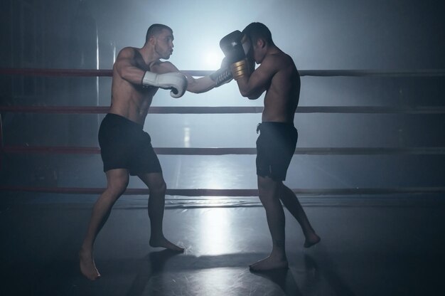 Two shirtless muscular man fighting Kick boxing combat in boxing ring