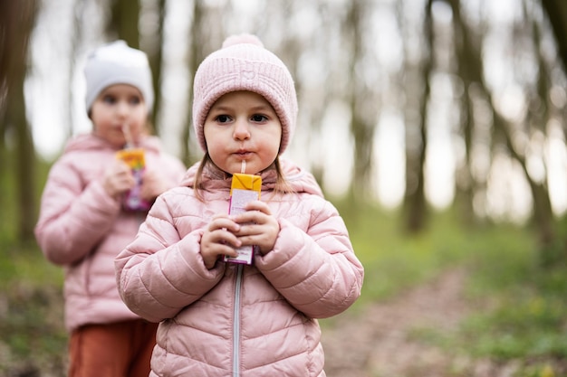 Two sisters drink juice using straws at forest happy child moments