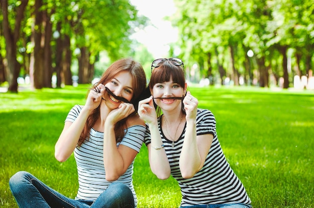 Two sisters, friends have fun, laugh, eat cotton candy, walk in a summer green amusement park. Happy