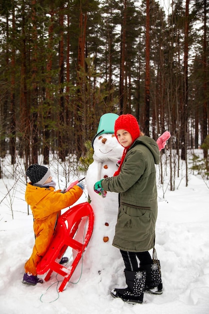 Two sisters make a snowman in winter