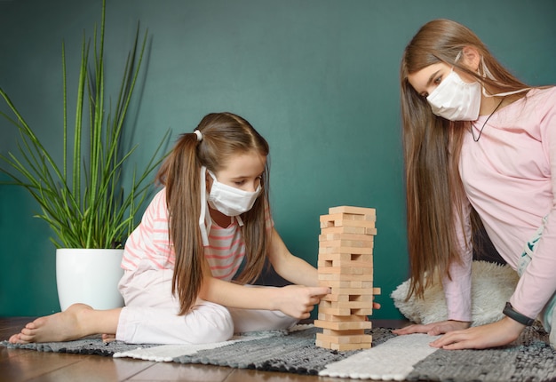 Two sisters in medical mask playing playing a blocks wood tower game