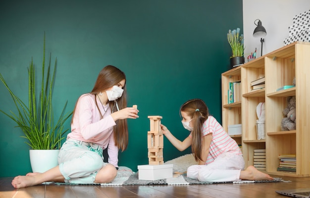 Two sisters in medical mask playing playing a blocks wood tower game