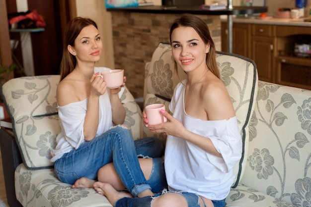 Photo two sisters on the sofa with a cups of tea in hands