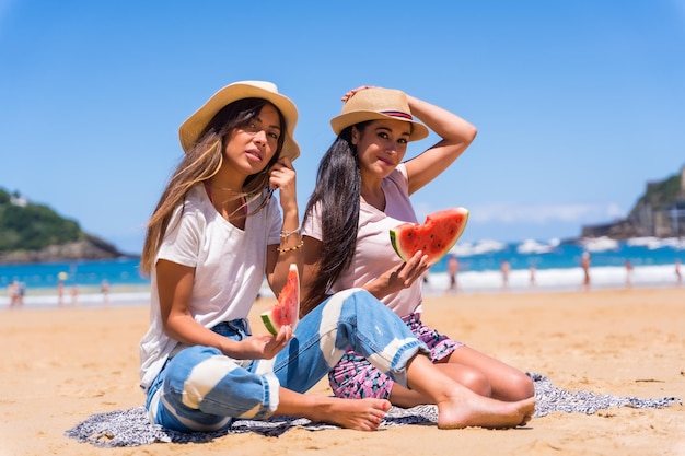 Two sisters in summer on the beach eating a watermelon enjoying the holidays with the sea in the background