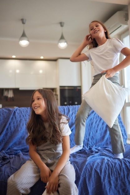 Two sisters wearing white pajamas fight with pillows and have fun concept of youth wellness and heal