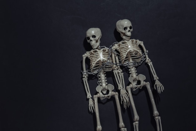 Two skeletons wrapped in chain on black dark background.