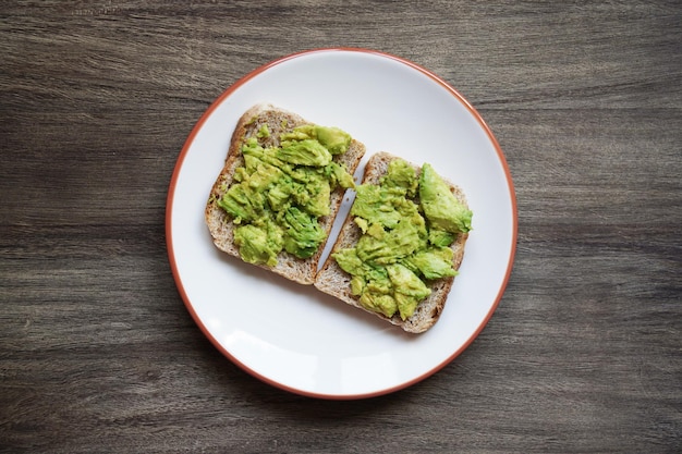 Two slices of avocado toast on a plate on rustic wooden table