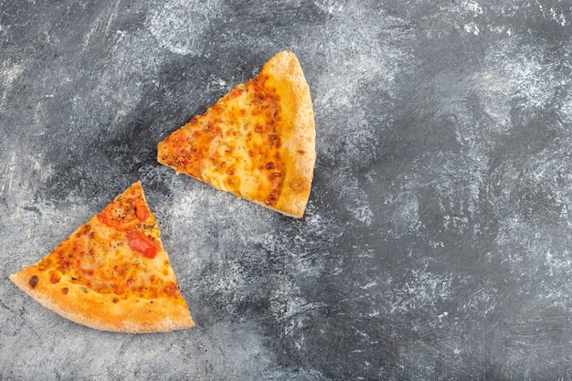 Two slices of delicious cheesy pizza placed on stone background. 