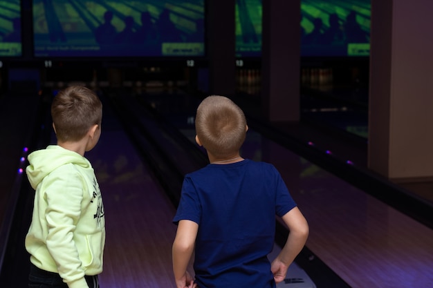 Two small bowling players are standing near the bowling alley