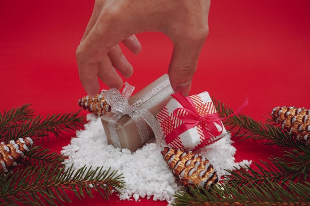 Two small Christmas gift boxes and pine branches and brown cones. A hand takes a gift