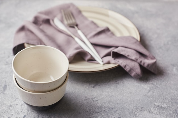 Two small empty salad bowls plates and linen napkins on gray background