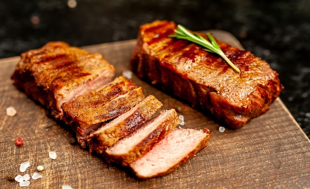 two small grilled beef steaks on a cutting board with spices on a background of black stone