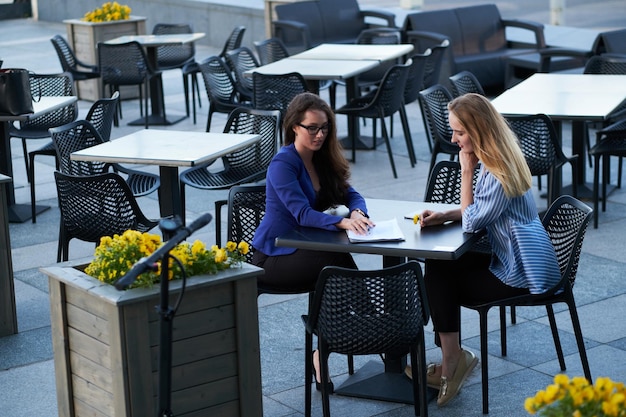 Two smart businesswomen are talking about their new project at small urban cafe outside.