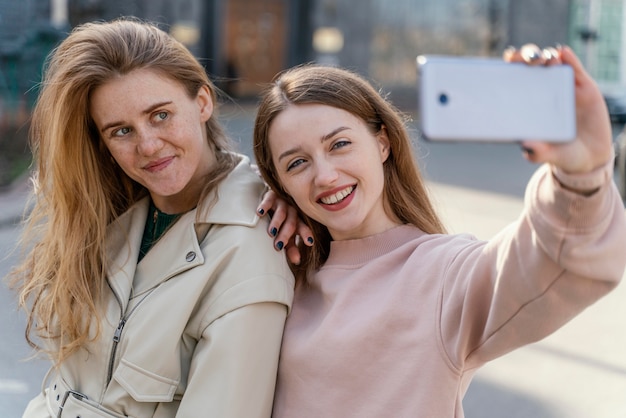 Two smiley female friends outdoors in the city taking a selfie