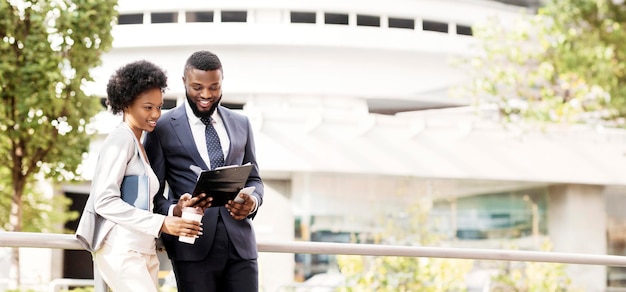 Two smiling african coworkers checking financial reports outdoors woman having coffee copy space