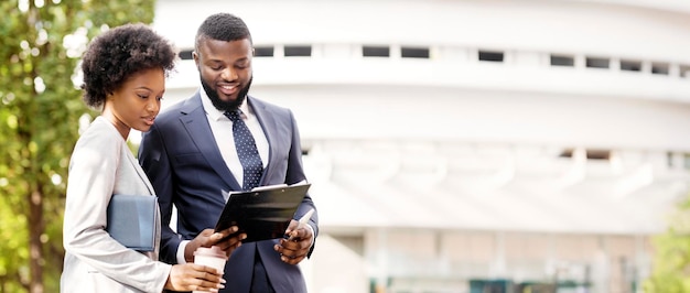 Two smiling african coworkers checking financial reports outdoors woman having coffee copy space