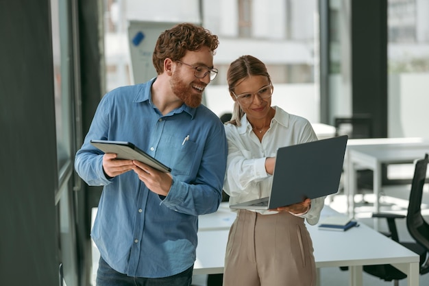 Photo two smiling business colleagues working together on project in office while use laptop