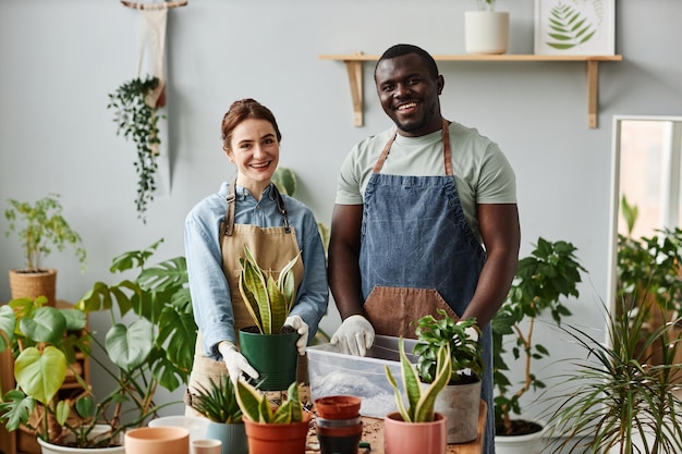 Two smiling gardeners looking at camera indoors posing with green plants