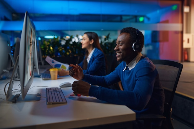 Two smiling managers works in night office. Cheerful male and female workers, dark business center interior, modern workplace