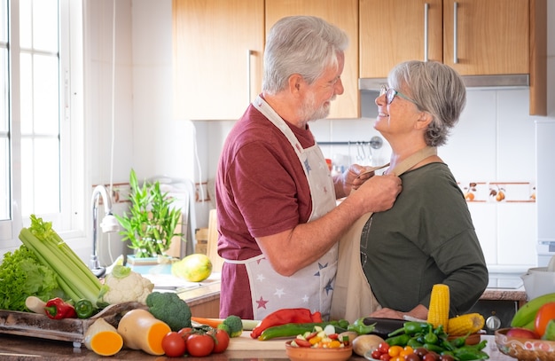 Two smiling seniors in the home kitchen prepare vegetables together for a healthy soup. Joyful elderly couple who appreciate a vegetarian lifestyle and enjoy their retirement