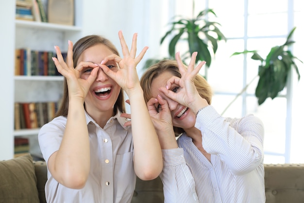 Two smiling women showing positive face emotions while siiting on sofa.