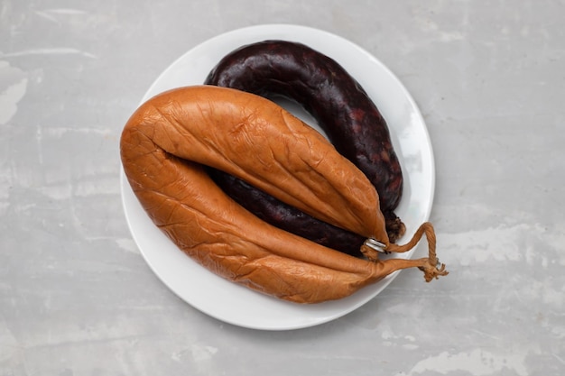 Two smoked sausages on white small dish on ceramic background