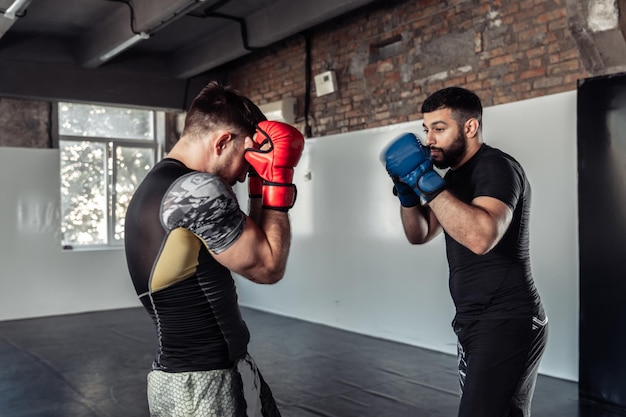 Two sparring partners of a kickboxer in boxing gloves practice kicks in a sports hall