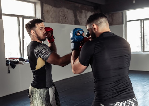 Photo two sparring partners of a kickboxer in boxing gloves practice kicks in a sports hall