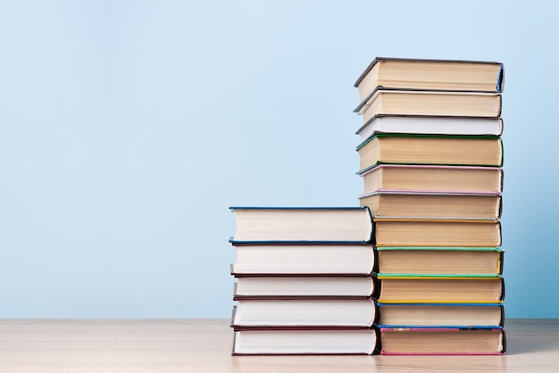 Two stacks of books of different heights stand on a wooden table against a light blue wall