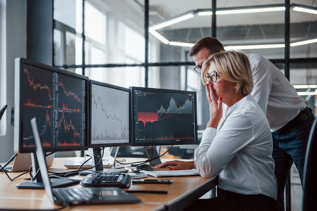 Two stockbrokers in formal clothes works in the office with financial market.