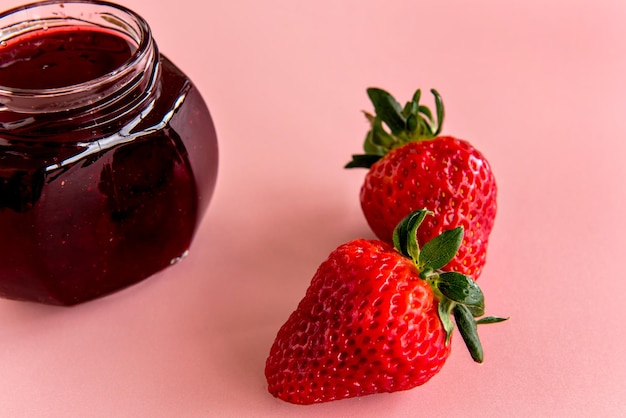 Two strawberries and strawberry jam on pink background