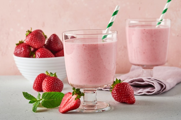 Two strawberry smoothie or milkshake with berries and mint in glass on light pink background. Summer drink shake, milkshake and refreshment organic concept. Healthy dieting, vegetarian food concept.