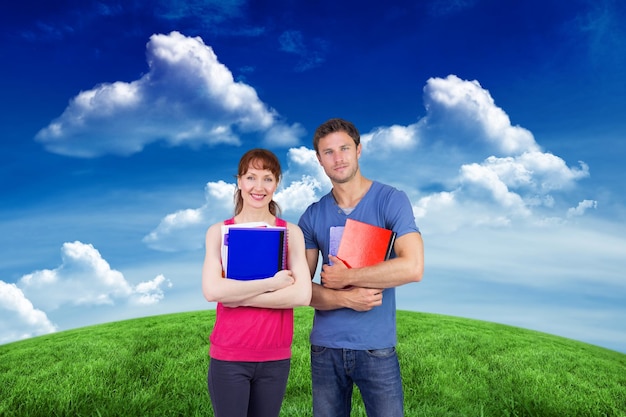 Two students both with notepads against green field under blue sky