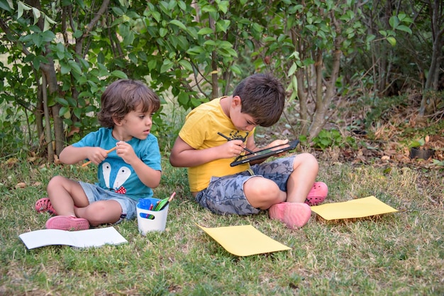 Two students lying in a park with their backpacks one of them writing in a notebook