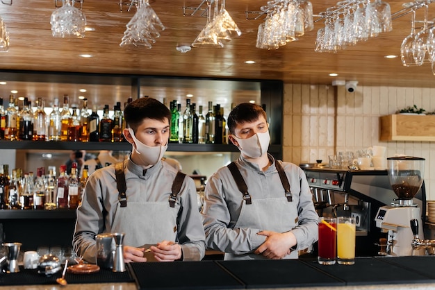 Two stylish bartenders in masks and uniforms are preparing cocktails at a party during a pandemic The work of restaurants and cafes during the pandemic