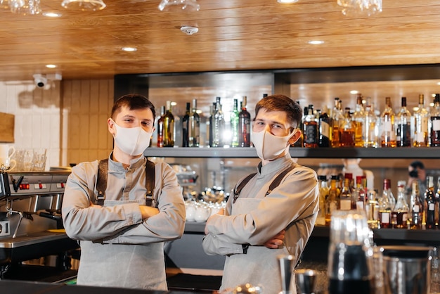 Two stylish bartenders in masks and uniforms during the pandemic stand behind the bar The work of restaurants and cafes during the pandemic