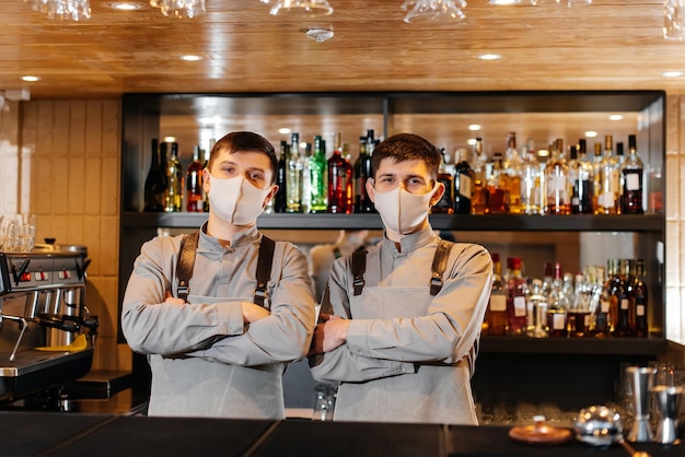 Two stylish bartenders in masks and uniforms during the pandemic stand behind the bar The work of restaurants and cafes during the pandemic