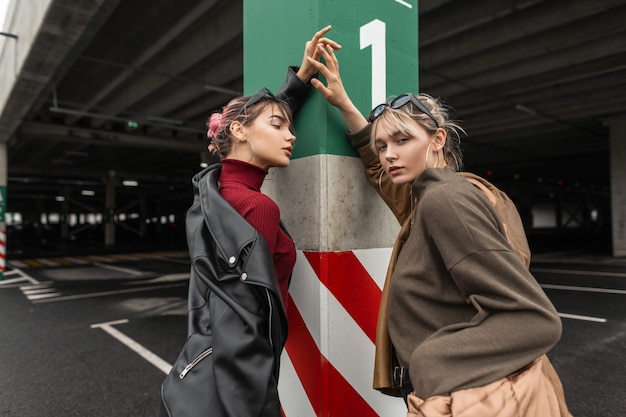 Photo two stylish cool young women in fashion autumn vogue clothes posing on a parking lot in the city