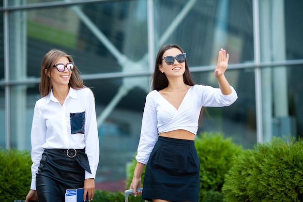 Two stylish female travelers walking with their luggage in airport