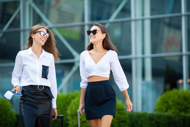 Two stylish female travelers walking with their luggage in airport